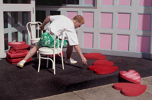 photo: Big man in green shorts working on a stack of red styrofoam hearts.