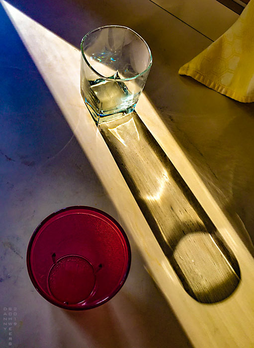 drinking glass and red plastic cup on sunlit countertop by Danny N. Schweers